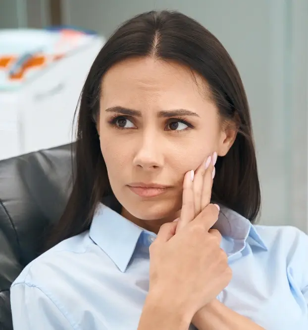 Woman with concerned expression touching her cheek, illustrating TMJ and orofacial pain symptoms.